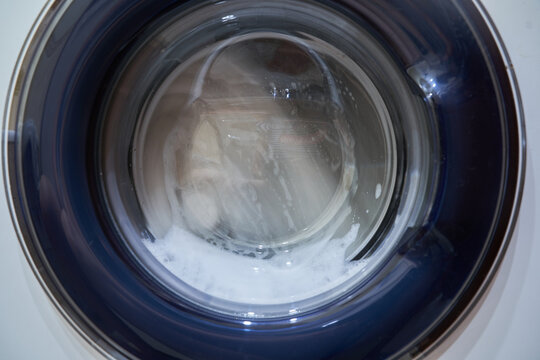Wet white laundry in the drum of the washing machine. Close-up glass door from the washing machine with space for copying. High quality photo