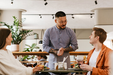 Smiling waiter serving couple in cafe