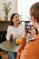 Man taking pictures of his girlfriend with mobile phone while having lunch together in cafe