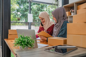 Friend muslim female work independent business sme online shopping working on laptop computer with parcel box on desk at home, SME online business and delivery concept
