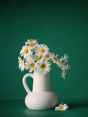 chamomile flowers in white jug on green background