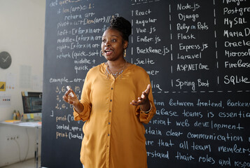 African American teacher standing near the blackboard with information and explaining new material...