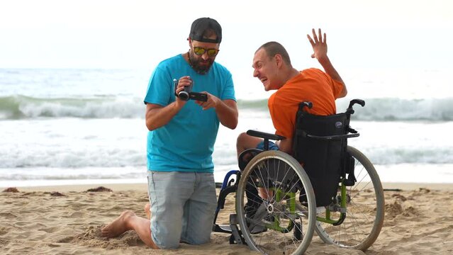 A disabled person in a wheelchair on the beach with a friend having fun taking a selfie