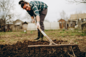 Young woman farmer works with a rake in a field in spring. Preparing the soil before planting....