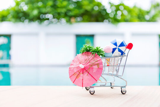 Summer decoration item in shopping card on swimming pool edge, outdoor day light, summer sale, Paper umbrella with coconut tree and ice cream in shopping cart - Powered by Adobe