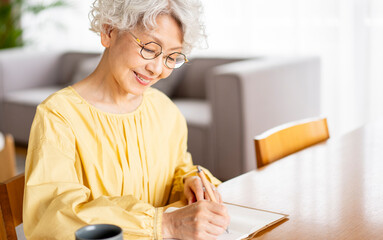 メガネをかけてノートに日記を書いているシニア女性