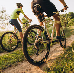A man and a woman ride bicycles on a dirt road in the summer at sunset. Active rest in the summer on bicycles.
