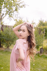 A little girl with long wavy hair in a beautiful pink dress is pranking and fooling around on the photographer's camera