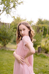 A little girl with long wavy hair in a beautiful pink dress is pranking and fooling around on the photographer's camera