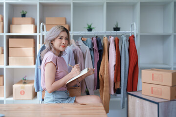 Portrait Of Asian Female Owner Of Fashion Store Checking Stock In Clothing Store With using notebook successful happy smile at small business, sme or ecommerce concepts