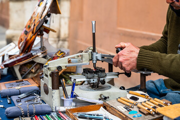 Elderly engraver at work on a street bench. Detail of the hands engrave plaques, pens and other...