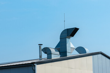 Metal exhaust ventilation pipes on the roof of a building under a blue clear sky.