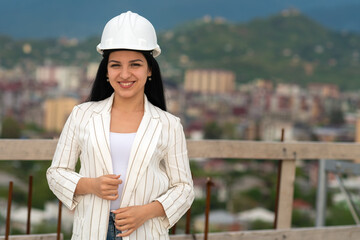 Smiling young female architect in a hard hat on a construction site, looking at the camera. Construction manager, manager, engineer at the construction site.