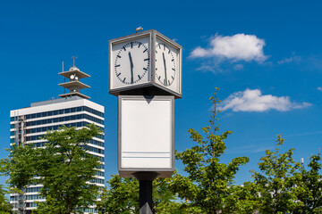 Street clock face with blank billboard against blue sky. Tall building with satellites on the roof in the background.