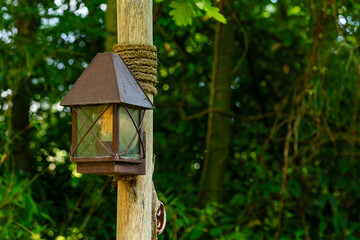 Old metal street lantern tied with ropes to a wooden pole. Close up.
