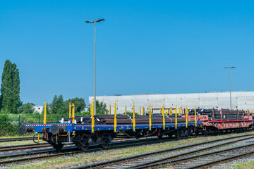 Railway platforms on the tracks loaded with bundles of metal pipes under a clear blue sky.