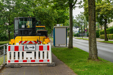 Fototapeta na wymiar A yellow excavator fenced with plastic in white and red barrier shields stands on the sidewalk.