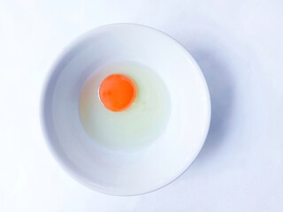 Raw chicken eggs in a bowl over white background. Perfectly round raw egg yolk. egg on white plate