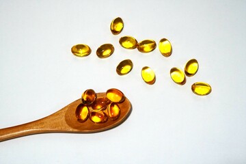Rice bran oil capsule on wooden spoon and white background.
