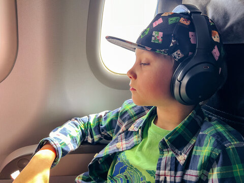 Caucasian Boy Travelling By Plane Listening To Music In Headphones Looking Outside At Aerial Sky View