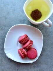 Pink macaroons on a white plate and buckwheat tea in a cup. Flat lay, top view