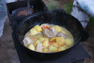 Food on the fire. Potatoes stewed with meat in a cauldron on the grill. Close-up. Selective focus....