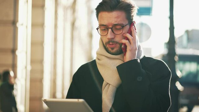 Stylish serious man walk down street in city with tablet in hands typing message, looking at screen, working or checking email. Entrepreneur, workaholic busy person, businessman, multitasking concept.