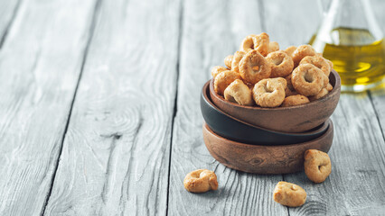 Traditional italian snack taralli or tarallini in wooden bowl over old gray wooden table. Rustic shot of taralli appetizer with copy space. Horizontal banner