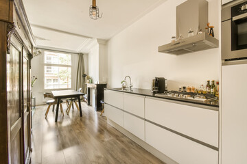 a kitchen and dining area in a small apartment with white cabinets, wood flooring and an open door leading to the patio