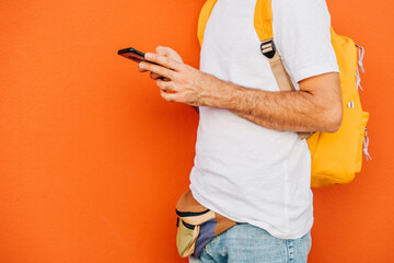Young men checking phone in front of orange background.