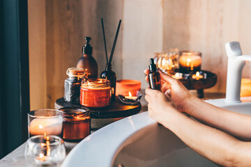 Essential oil bottle standing at beautiful hot tub bath with candles. Beauty and spa concept.