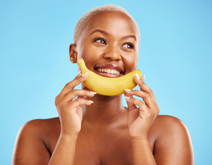 Beauty, smile and banana with a model black woman thinking on a blue background in studio. Skincare, idea and food with a happy young female person holding yellow fruit for natural wellness or detox