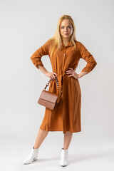 Blonde woman in an elegant casual brown dress with a women's handbag.