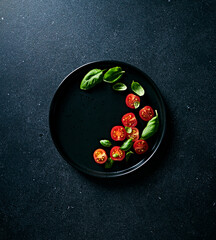 Cherry tomatoes and basil leaves on black ceramic plate. Copy space. Top view