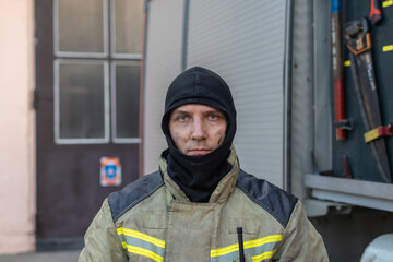 Portrait of a tired firefighter in a protective suit standing by the fire engine after returning to...
