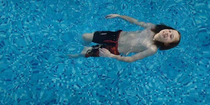 boy swims in the pool, in shorts, top view, blue water