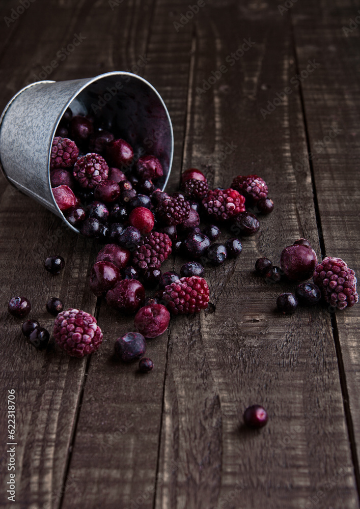 Wall mural frozen berries mix in a black bowl on wooden background. still life photography