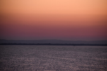 Sunrise sunset orange purple blue pink skies over ocean sea with mountains and beach on horizon line