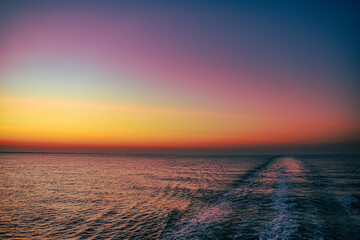 Sunrise sunset orange purple blue pink skies over ocean sea with boat trail 