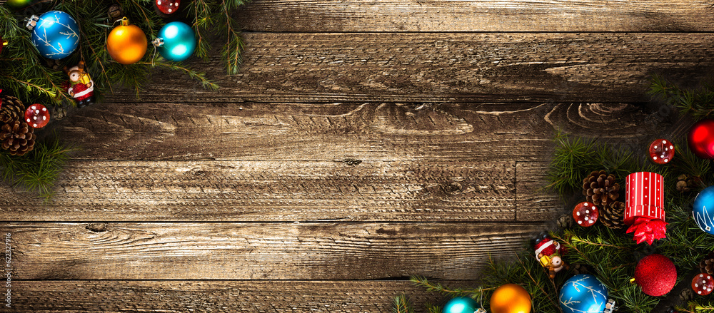 Wall mural Merry Christmas Frame with real wood green pine, colorful baubles, gift boxe and other seasonal stuff over an old wooden aged background