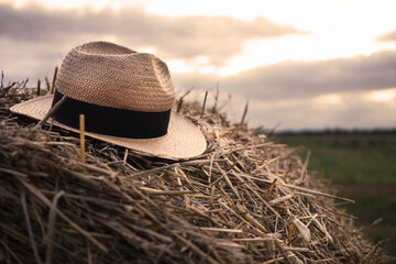 Summer hat on a haystack against the background of clouds and the setting sun