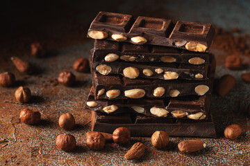 Dark and milk chocolate with nuts on a dark background sprinkled with cocoa powder.