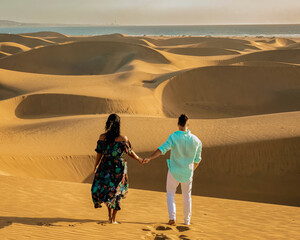 couple walking in the sand dunes desert of Maspalomas Gran Canaria, men and women watching sunrise...