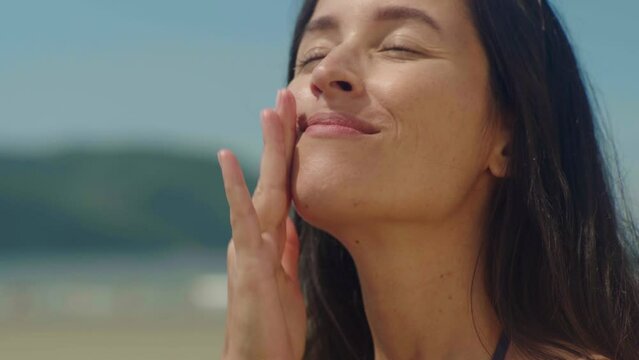 Close-up woman on bikini takes sunscreen of tube, moisturizing lotion applies sunblock on her face
