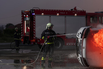 Fototapeta premium Firefighters fight the fire flame to control fire not to spreading out. Firefighter industrial and public safety concept. Traffic or car accident rescue and help action. 
