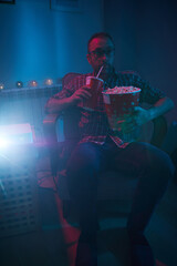 Obraz premium Man enjoying popcorn and juice while watching movie at home projector.