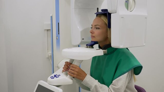Tracking shot of blonde female patient standing taking 3D panoramic teeth x-ray with digital dental x-ray machine in modern dentistry clinic, slow motion. Treatment and prevention. Healthcare, medical
