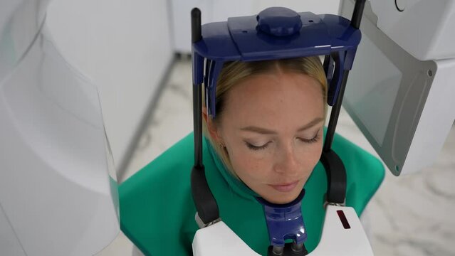 Closeup high-angle view of young female patient standing in dental x-ray machine for dental radiography. Concept of dentistry, medicine, healthcare, jaw scanning. Shooting in slow motion.