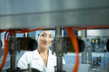 Female scientist in white coat and blue hat working in the control  machine of production line.