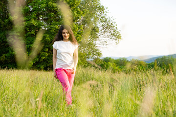 Naklejka na ściany i meble A young woman walks across a field. A walk in nature in the summer.